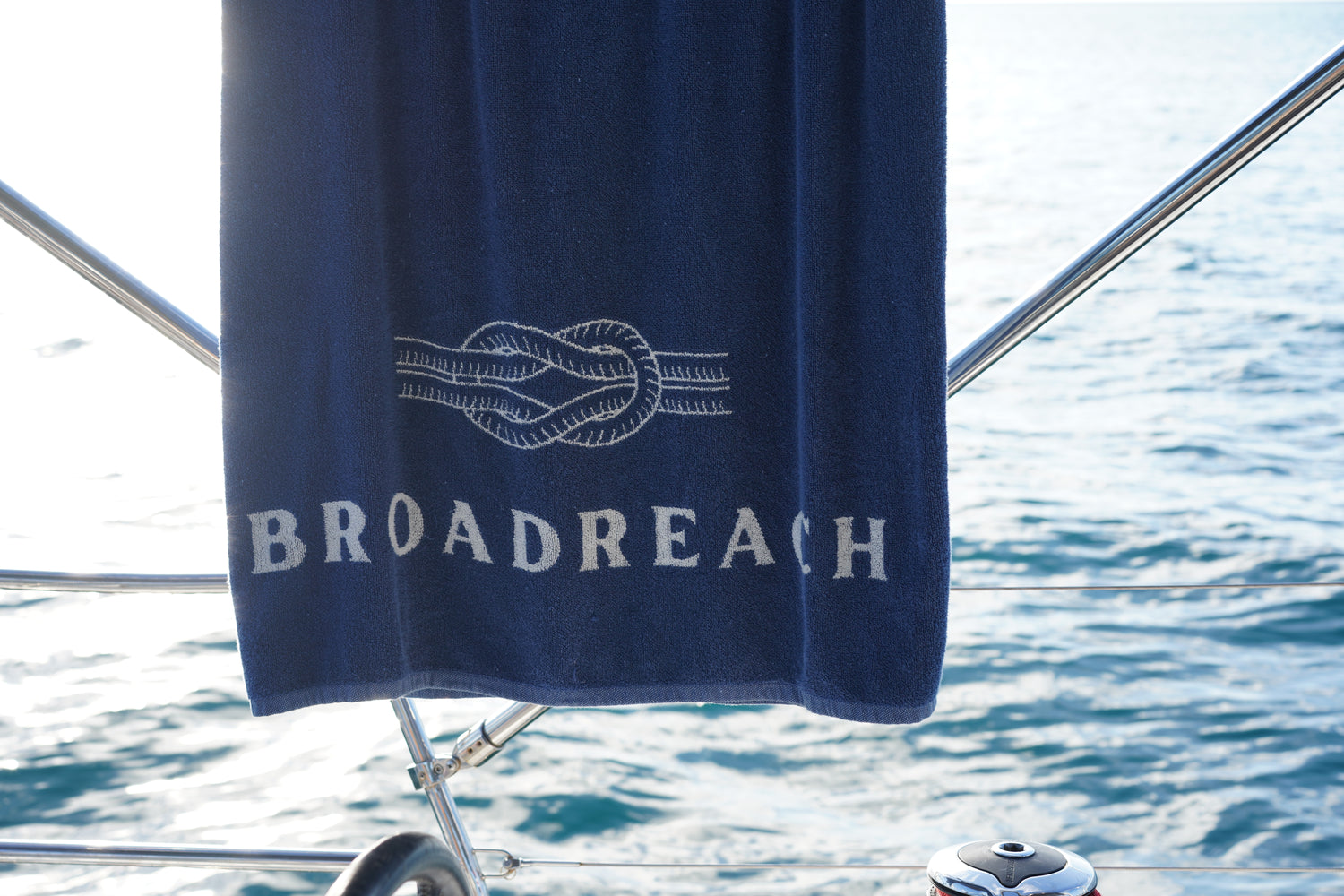 Image of Poolside towel by BroadReach resort wear hanging on rail of yacht with ocean in background.