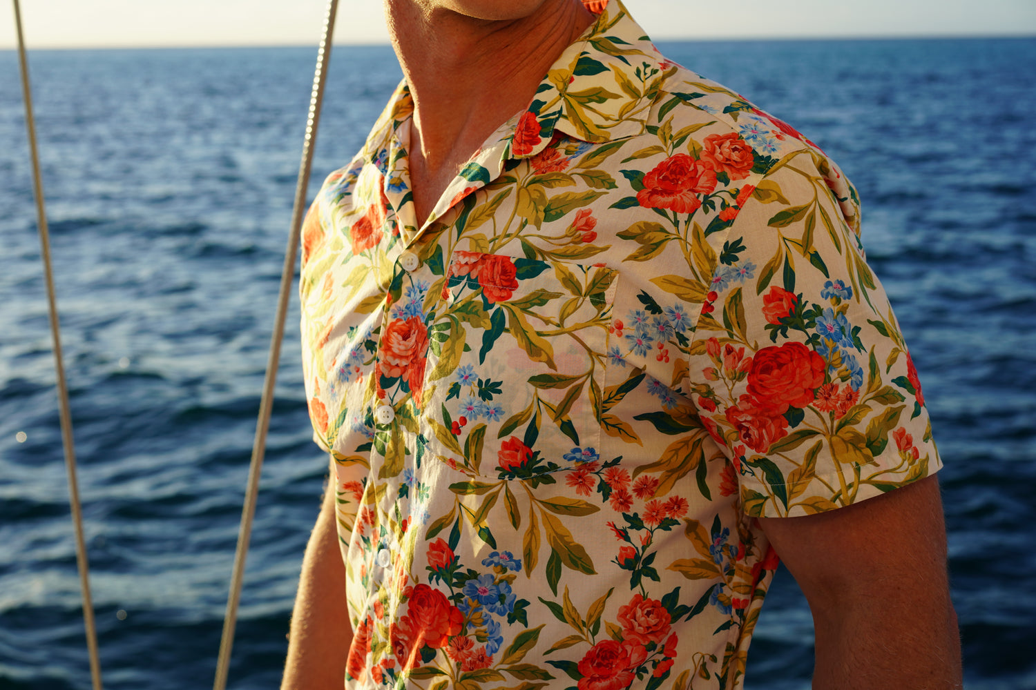 Image of man standing on yacht with ocean in background wearing BroadReach resort wear Helmsman short sleeved button-up shirt in Liberty Fabrics Matilda Bloom print.