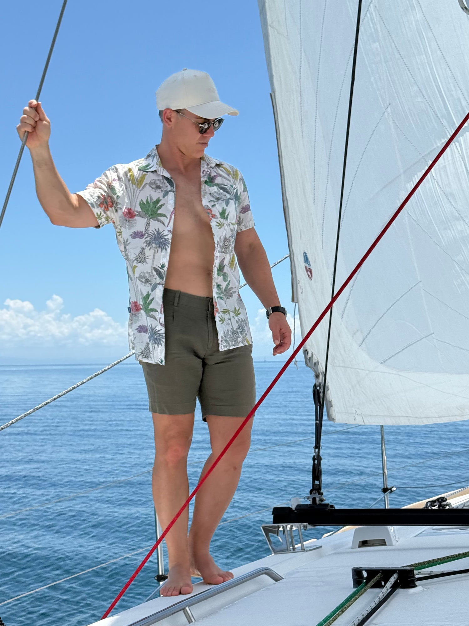 Image of man standing on yacht with ocean in background wearing BroadReach resort wear Helmsman short sleeved button-up shirt in Liberty Fabrics Darwin’s Journey print and BroadReach Sundowner cap in sand color.
